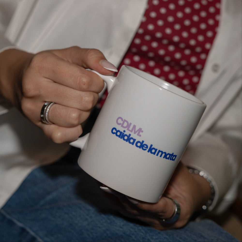 Two white ceramic mugs with printed logos, held by people in a casual indoor setting. One mug shows the text 'HDP hertabandi' and the other shows 'CDLM caida de la mata'.